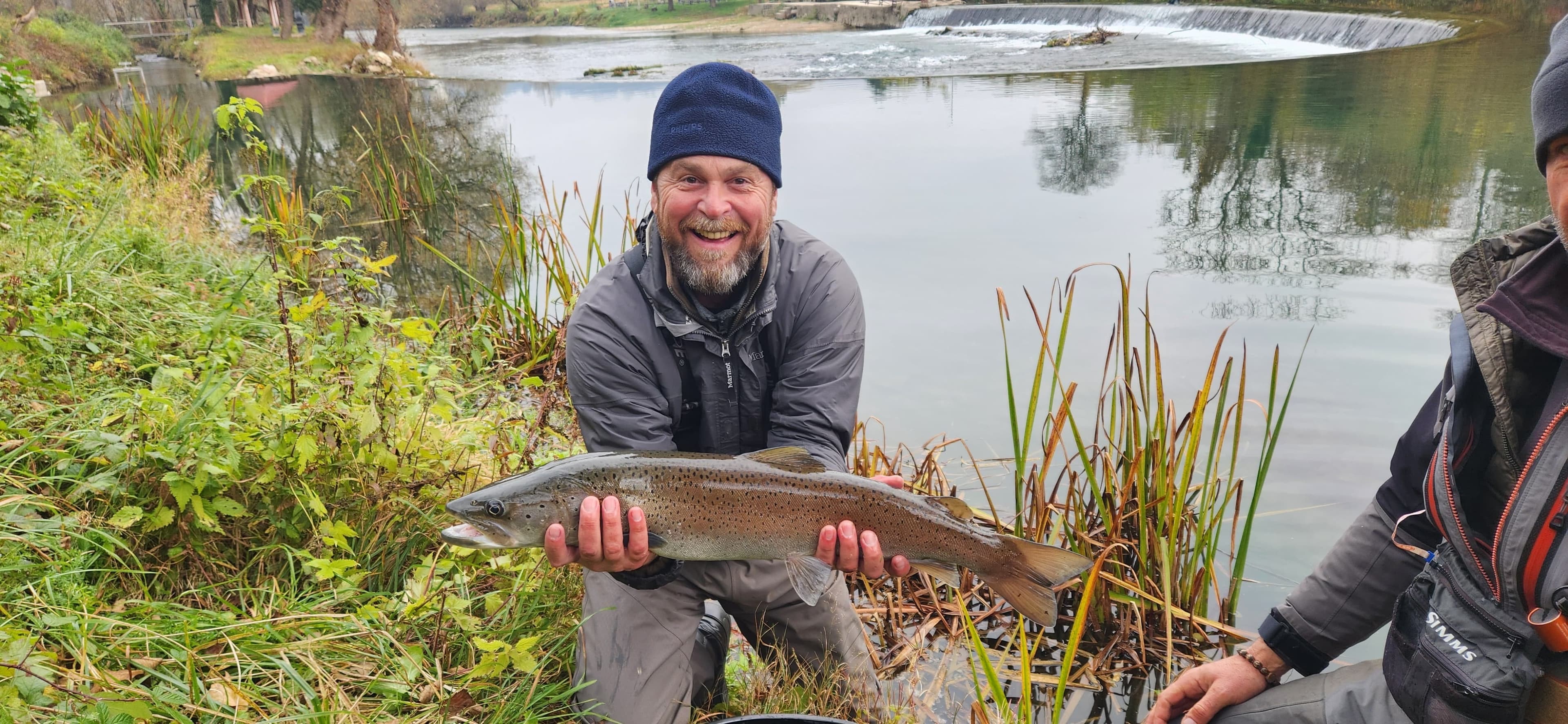 Angler holding a huchen beside a weir with still water reflections